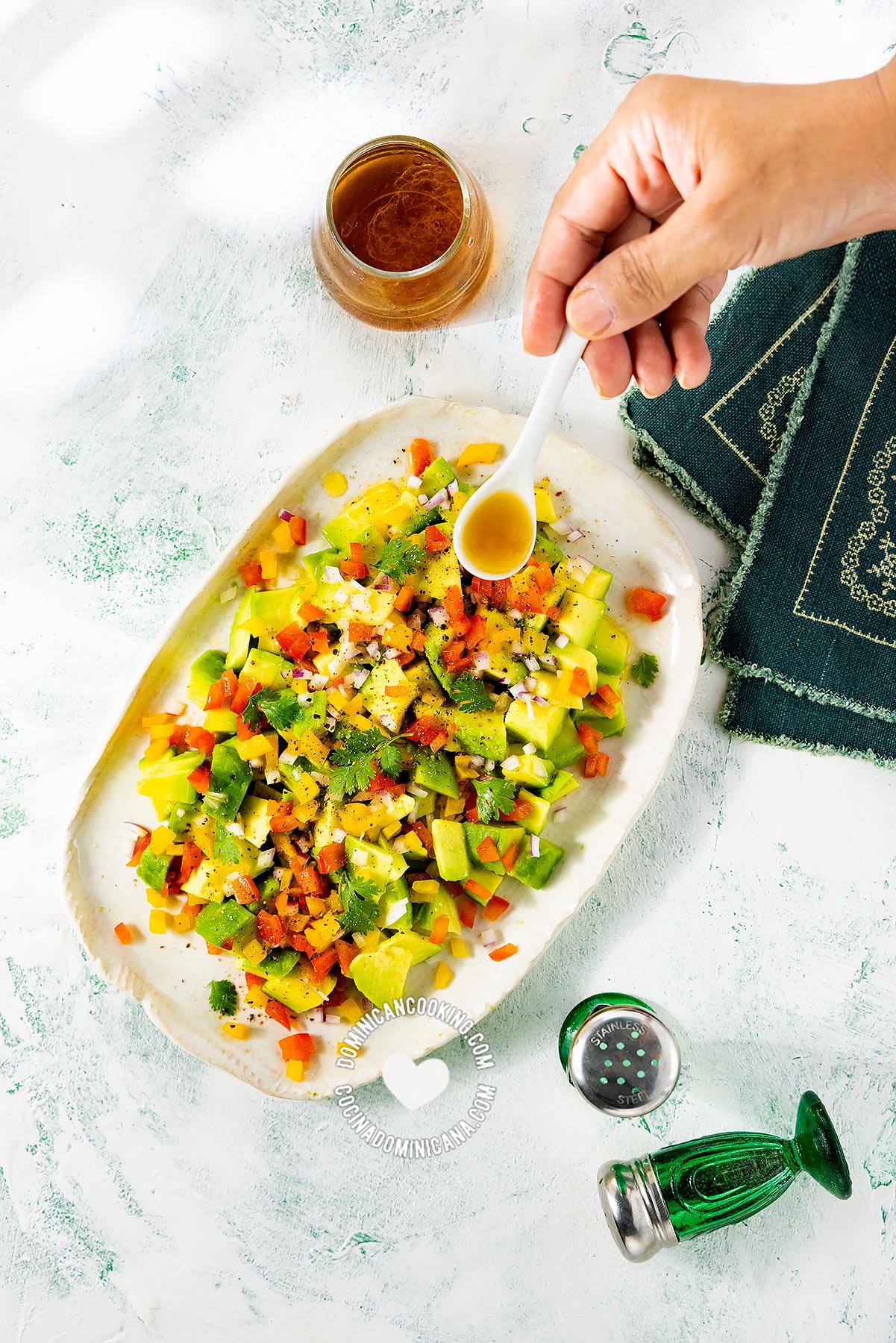 Hand pouring vinaigrette on Ensalada de Aguacate (Avocado Salad)