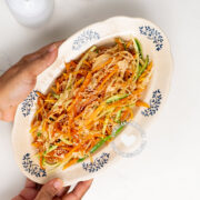 Hands holding plate with green papaya salad